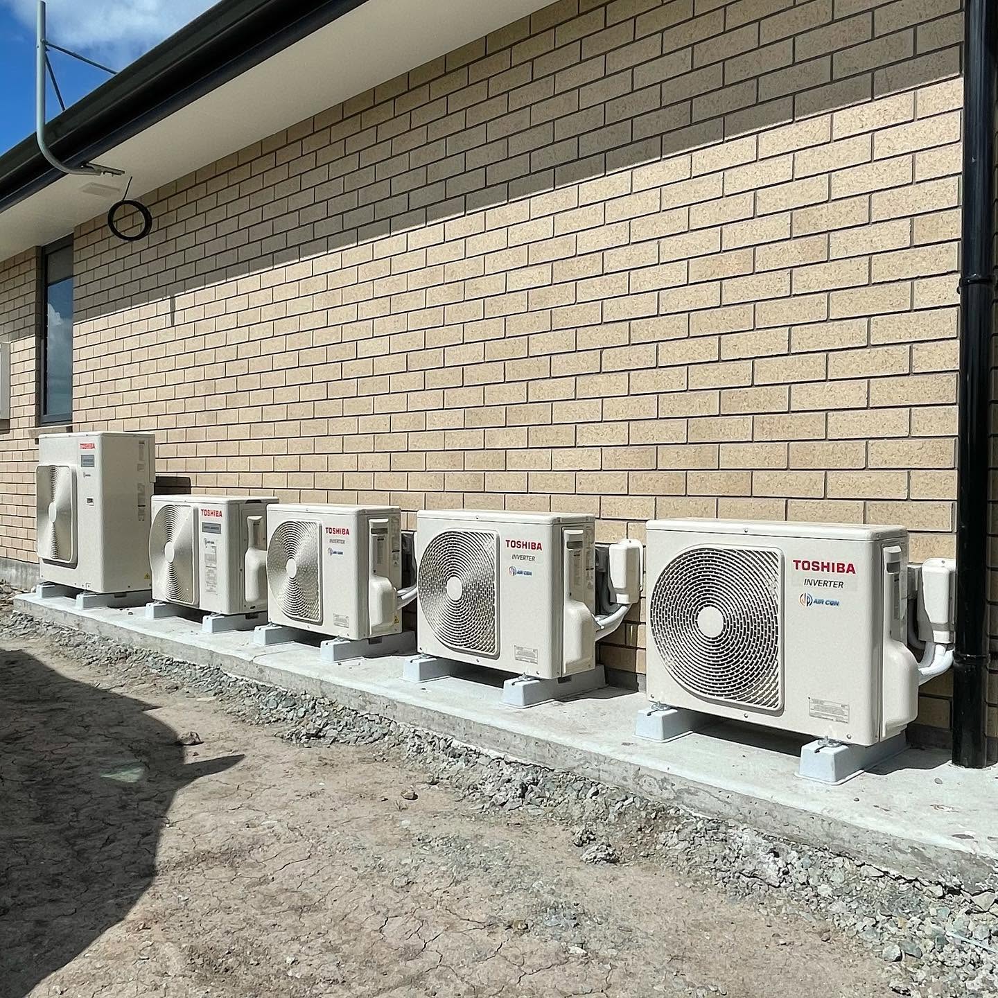 Row of Toshiba heat pump outdoor units installed along a brick wall